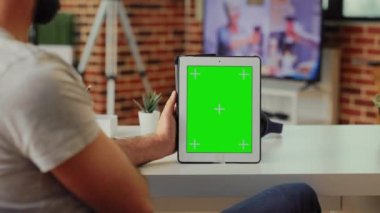 Çalışan, evdeki modern tablet üzerinde yeşil ekranı analiz ediyor, izole edilmiş krom anahtar telif alanı şablonuna sahip dijital cihazlar tutuyor. Taşınabilir aygıttaki boş model arkaplana bakıyorum.