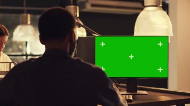 Bilgisayarda yeşil ekran görüntüsüne bakan serbest yazar, bilgisayar ekranında boş model şablonu ve telif uzayı ile çalışıyor. Ofiste günbatımında izole edilmiş krom anahtar arkaplanı analiz ediliyor.