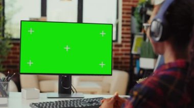 Kulaklıklı bir bayan öğrenci yeşil ekran ekranına bakıyor, kulaklıkla müzik dinliyor ve izole bir model şablonuyla çalışıyor. Bilgisayar monitöründe krom anahtar kopyalama uzayı kullanılıyor.