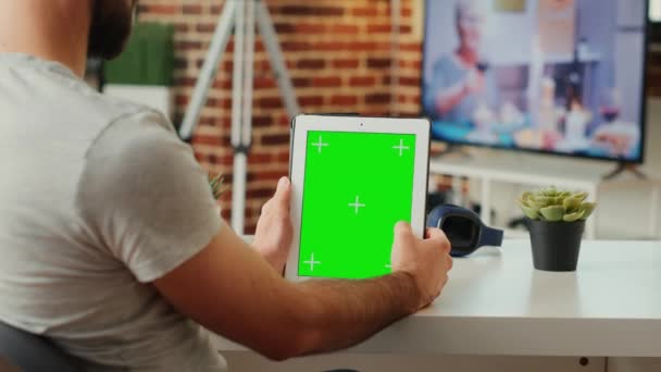 年轻人在客厅里垂直地拿着带有绿屏模板的数码平板电脑 坐在办公桌前 使用独立的彩色键显示与复制空间和模拟背景 屏幕应用程序 — 图库视频影像