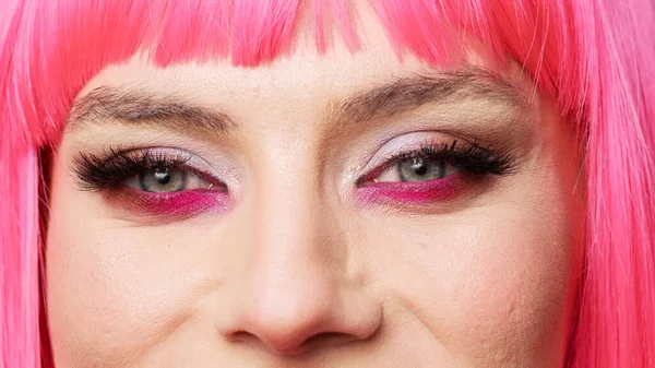 Macro shot of attractive woman with beautiful eye makeup and pink hair posing in studio, having fun and feeling confident. Healthy positive beauty model with big eyelashes. Extreme closeup.