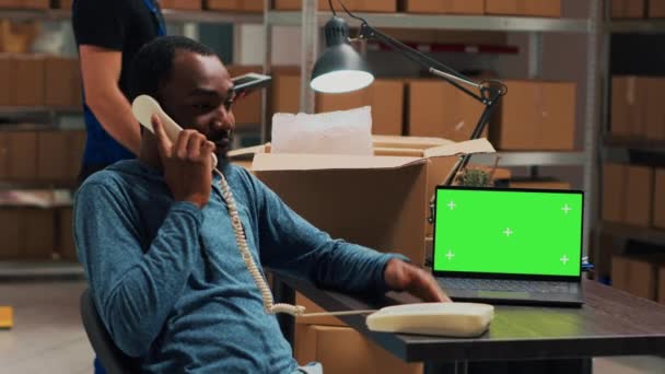男性起業家は 固定電話で話し Pc上の緑の画面を使用して 倉庫で隔離されたクロマキーディスプレイと協力しています 電話と空白のコピースペースを持つ店舗の所有者 — ストック動画