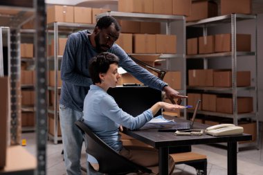 Depo çalışanları teslimat listesini dizüstü bilgisayarda analiz ediyorlar. Nakliye paketinden önce metal kutu siparişi arıyorlar. Ulaşım lojistiğinde çalışan çok ırklı ekip