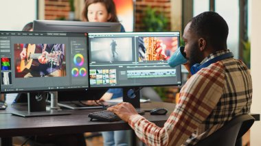 Afrika kökenli Amerikalı çalışan, multimedya yazılımında video içeriğini düzenliyor, odak ışığı ve renk derecelendirme kullanılarak. Erkek film yapımcısı pc multi monitörlerinde film montajı üzerinde çalışıyor.
