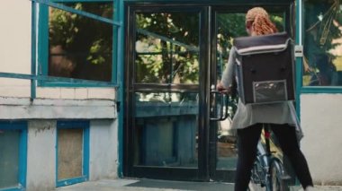 Afrikalı Amerikan kuryesi, bayan müşteriye kese kağıdı veriyor. Restoran paketini bisikletle getiriyor. Carrier 'dan hazır yemek alan kadın, binanın girişinde oturuyor..