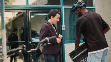 Kadın müşteri, yemek siparişini kredi kartıyla ödüyor. Kadın, fast food yemeği için ulaşılamaz ödemeler yapıyor. Sırt çantalı teslimat kuryesi. El kamerasıyla..