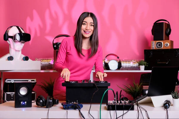 スタジオでプロミキサーコンソールを使用してピンクの背景にテクノ曲を再生しながらDjテーブルに立つアジアのパフォーマーの肖像画 夜にクラブで音楽を演奏することを楽しむアーティスト — ストック写真