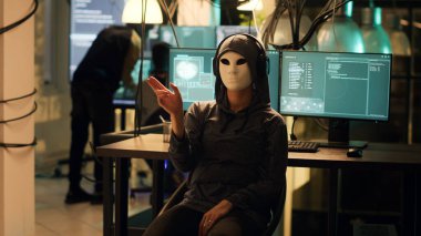 Female hacker with anonymous mask using hologram to break into firewall encryption, holographic illegal hacking concept. Masked dangerous thief using augmented reality to hack system. clipart