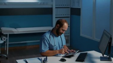 Uygulamalı asistan elinde tablet bilgisayarla gece geç saatlere kadar hastane ofisinde çalışırken hasta hastalıkları raporunu analiz ediyor. Tıp alanında uzman bir erkek hemşire. İlaç servisi.