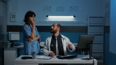 Doktor ve hemşire gece geç saatlerde muayenede hasta raporlarını tartışan bilgisayarlardaki tıbbi uzmanlıkları analiz ediyorlar. Sağlık hizmeti ve konsept