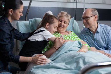 Hasta büyükanneyi hastane ziyaretinde kucaklayarak karşılayan mutlu küçük kız. Yaşlı kadın tıp yatağında uzanıp yaşlı hasta kliniğinde torununa sarılıyor..
