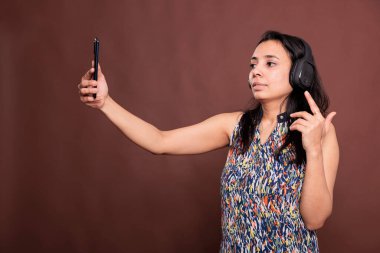 Kulaklıklı Hintli bir kadın akıllı telefondan video görüşmesi yapıyor, telekonferansta konuşuyor. Kablosuz kulaklık takan, cep telefonu tutan, uzaktan iletişim kuran, online görüşme