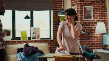 Depresyondaki kadın çamaşırları ütülemekten sıkılmış, ev işlerini yapan stresli bir ev hanımı. Genç yetişkin bahar temizliği ve ev işlerini yalnız yaptığı için üzgün hissediyor..