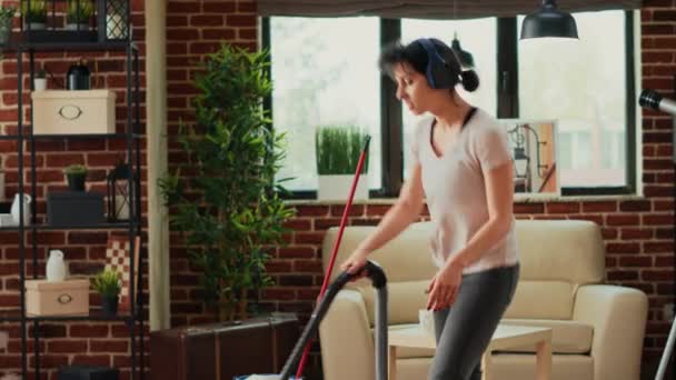 女人们在耳机和吸尘器地板上听音乐 玩吸尘器 年轻的现代女人在做春季清扫家务的时候感到快乐 — 图库视频影像