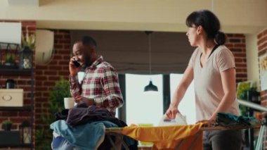 Kızgın kadın rahatlamış adama gömlek fırlatıyor, erkek arkadaşının ev işlerine yardım etmemesinden rahatsız oluyor. Stresli bir yetişkin hayat arkadaşına kızıyor, evde bahar temizliği yapıyor. El kamerasıyla..