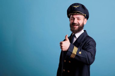 Gülümseyen uçak pilotu, baş parmağı havada profesyonel üniformalı bir portre giyiyor, uçak kaptanı kameraya bakıyor. Havacı parmağıyla onay işareti gösteriyor, stüdyo resmi.