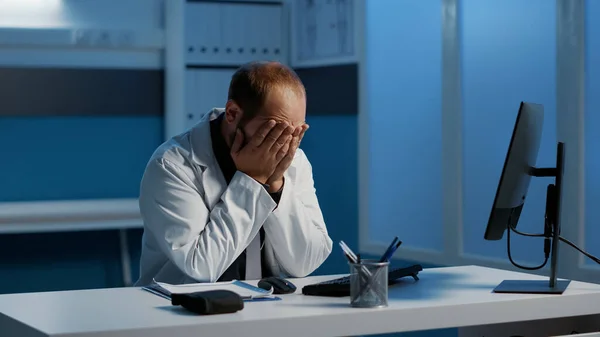 疲れ切った医師の男性は 病院のオフィスで働く夜のシフトは コンピュータ型医療報告書に医療専門知識を分析します ストレスを受けた医師が患者治療計画を立てる — ストック写真
