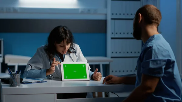 General practitioner showing medical expertise to nurse using tablet computer with green screen chroma key template. Clinical staff working over hours in hospital office, planning health care report