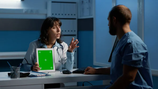 アシスタントと患者レポートを議論しながら 緑の画面クロマキーディスプレイを指してタブレットコンピュータを保持医療 病院の医療専門知識で夜間勤務の臨床スタッフ — ストック写真