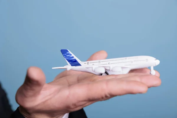 Close up of aviator holding plane toy in hands, playing with commercial passenger jet model . in studio shot with blue background. Aircraft flying concept, professional aviator,