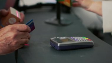 Erkek müşteri ilaç parasını ödemek için kredi kartını kullanıyor. Eczane tezgahında ücretsiz ödeme yapıyor. Kutular dolusu ilaç ve hap alan, reçeteli ilaç tedavisi gören biri. Kapat..