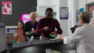 Afro-Amerikalı müşteri vitaminlere NFC ödemesiyle ödeme yapıyor, posizyon terminalini eczaneden takviye ve ilaç almak için kullanıyor. Eczane masasında erkek müşteri var..