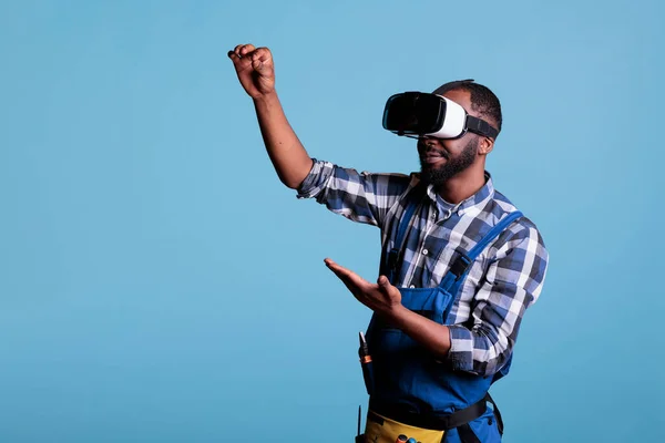 Experienced renovator using virtual reality goggles looking at plans for new kitchen project. Construction worker using vr headset against blue isolated background.
