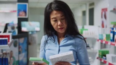 Female customer examining boxes of drugs on drugstore shelves, looking to buy prescription treatment and pharmaceutical healthcare products. Client checking supplements package leaflet.