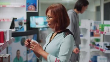 Asian woman reading cardiology pills boxes on shelves, searching for healthcare medicine. Female customer checking pharmaceutics package in drugstore, medical supplies and vitamins.