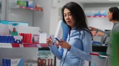 Kadın müşteri vitamin paketlerini analiz ediyor, vitamin aminleri, hastalık tedavisi ve ilaveler arıyor. İlaç almak için kutu kutu hap okuyan Asyalı bir kadın. El kamerasıyla..