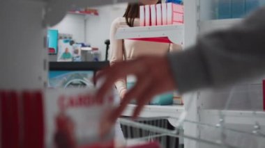 Female customer examining packages of medicaments on shelves in pharmacy, looking for prescription medicine and pharmaceutical products. Woman checking medical supplements and vitamins.