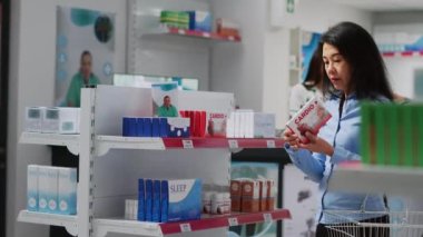 Female customer analyzing pakages of medicine on shelves, looking for disease treatment and supplements. Asian woman reading boxes of pills leaflet to buy healthcare medicaments.