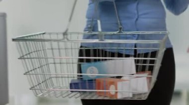Female client putting boxes of medicine in basket, buying pharmaceutical products or supplements from shelves. Woman looking at packages of pills and vitamins, taking medicaments. Handheld shot.