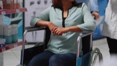 Engelli ve bakıcı olan bir müşteri eczacıya haplardan ve ilaçlardan bahsediyor. Tekerlekli sandalyedeki Asyalı müşteri eczaneden ilaç alıyor. El kamerasıyla..