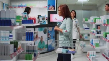 Drugstore assistant helping customer with pills treatment and medicine in pharmacy shop, specialist explaining prescription drugs or vitamins. Client and employee looking at medicaments box.