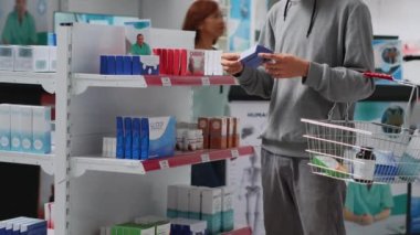 Male customer looking at medicaments boxes in drugstore, searching for medical treatment and vitamins. Asian adult analyzing packages of pharmaceutics before buying supplements or pills.