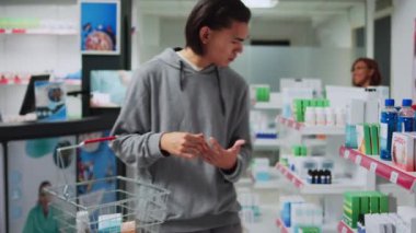 Tıbbi mağazada eczane broşürlerini açıklayan Asyalı işçiler, reçeteli tedavi ve ilaç ürünleri bulma tavsiyesinde bulunuyorlar. Genç adam raflardaki vitaminlere ve ilaçlara bakıyor..