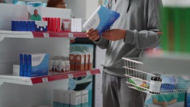 Eczanedeki ilaç kutularına bakan genç adam tıbbi tedavi ve vitamin arıyor. İlaç almadan önce Asyalı yetişkinler ilaç paketlerini inceliyor..