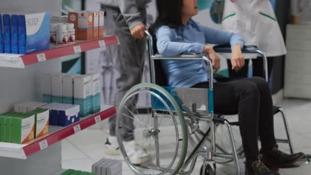 アジアの障害者は 男性のソーシャルワーカーや薬剤師と話をしながら 薬を購入しようとしています 女性の車椅子のユーザーは 専門医薬品からの助けを受けて — ストック動画