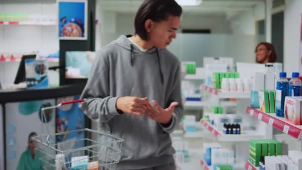 アジアの労働者は 医療小売店舗で薬局のチラシを説明し 処方治療や医薬品を見つけるためのアドバイスを与えます 棚の上でビタミンや薬を見ている若い男 — ストック動画