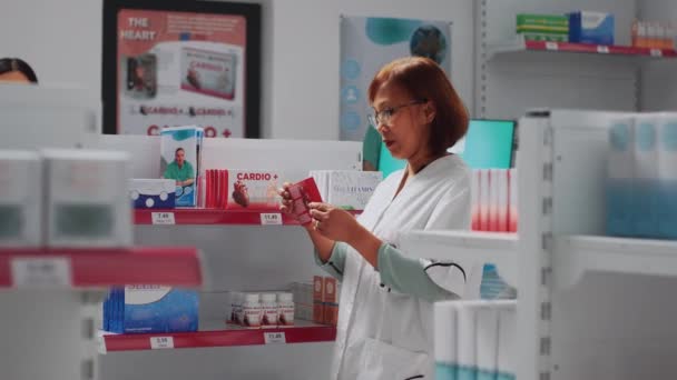 女性薬剤師は お客様を助けるために準備し 店舗棚に医療製品を配置します アジアのコンサルタントは薬とビタミンの箱を見て薬のパッケージをチェック — ストック動画