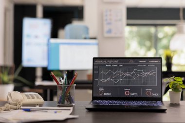 Empty office at the beginning of the working day, partial view of work station. Annual growth report on portable computer, graphs printed on table for next days staff meeting.