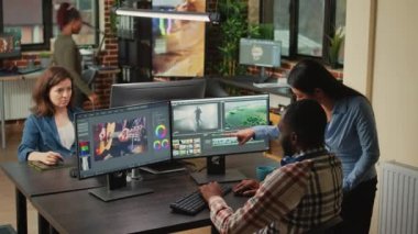 Diverse videographers editing creative film montage on software, brainstorming ideas to improve focus and lighting. Man and woman working with post production video and audio footage.