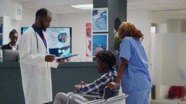 Physician consulting male wheelchair user with impairment, meeting in facility waiting area. Nurse helping man with chronic disability in clinic, checkup visit exam appointment.