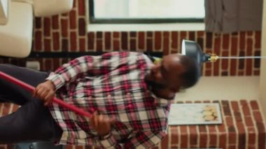 Vertical video: Cheerful man mopping apartment floors and listening to music, acting silly with dance moves at home. Young happy person doing spring cleaning with mop, having fun and smiling. Tripod