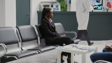 Health specialist consulting female patient in hospital waiting room, talking about disease diagnosis and treatment. Medical assistant showing report notes to woman with illness.