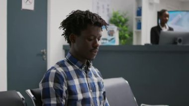 Male patient waiting to attend consultation with doctor, sitting in hospital reception. Young adult in waiting area having checkup exam appointment with specialist to cure disease at health center.