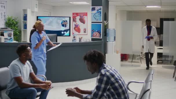 アフリカ系アメリカ人患者 病院のロビーエリアで待っている病気の人々との協議を行う医療専門家 予定に出席する前に待合室に座っている男性のグループ — ストック動画
