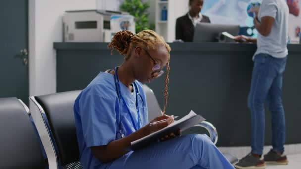 待合室 施設ロビーエリアに座っている医療補助者の診断フォームを分析します 健康センターで健康診断の予約をする前に報告書を見る若い医療専門家 — ストック動画