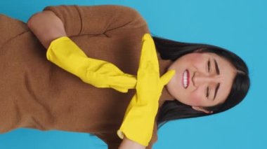 Vertical video: Asian homemaker doing time out gesture during house cleaning in studio over blue background. Tired housewife needed pause from work, used only the best cleaning products and equipment